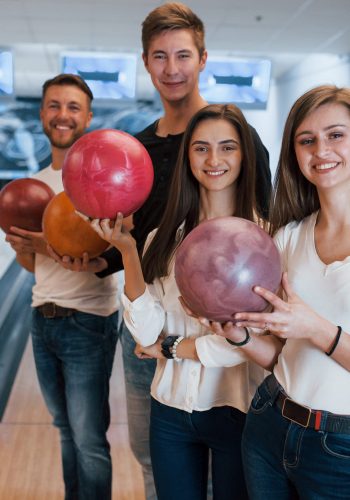 Standing against playing area. Young cheerful friends have fun in bowling club at their weekends.